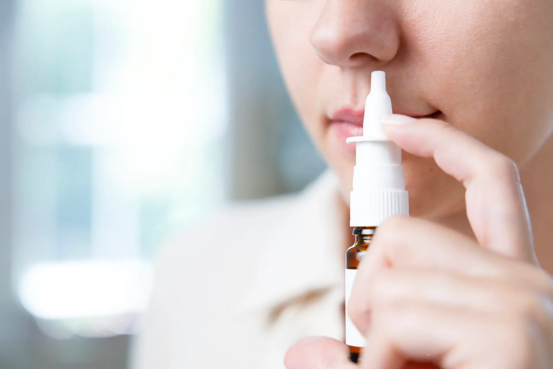 Close-up shot of sick young woman using nasal spray